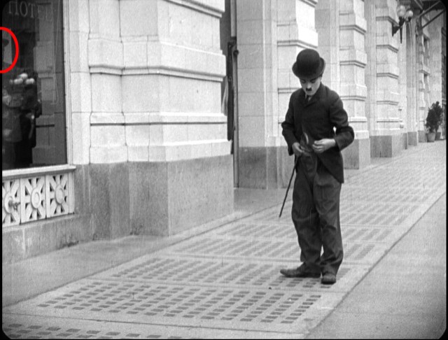 We're watching Charlie, and so is the man in the hat, watching him through the window in The Bank.