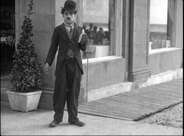 A large crowd gathers to watch Charlie - anticipating what will happen with the banana in By The Sea (1915). Filmed in Venice 